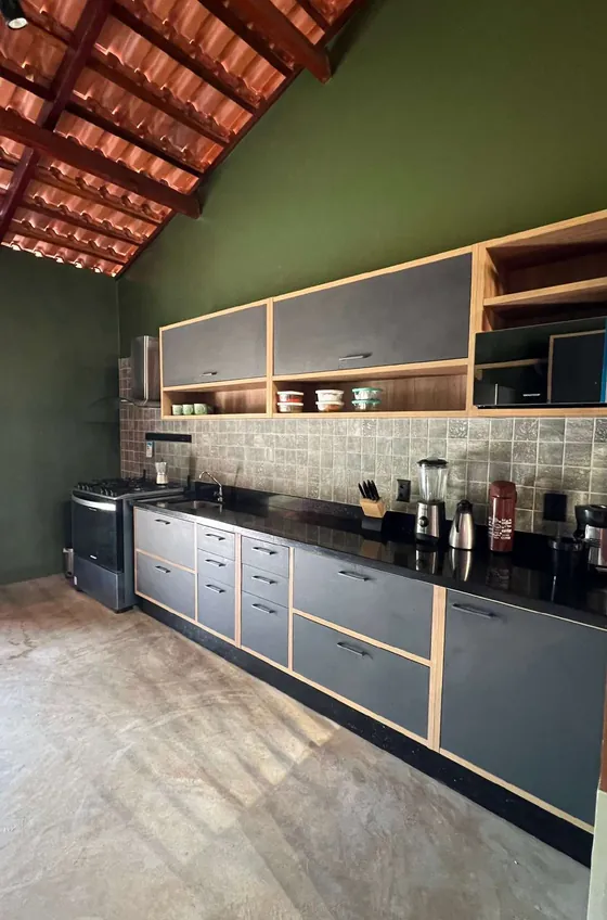 Cozinha com parede verde, armários cinza com contorno de madeira e telhado aparente