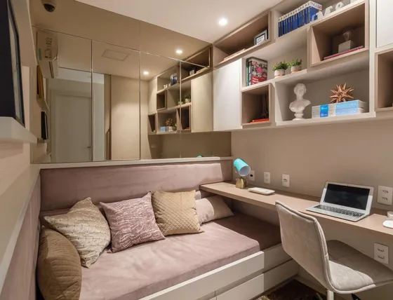 Home office com sofá-cama rosé, bancada de estudo e estante com nichos