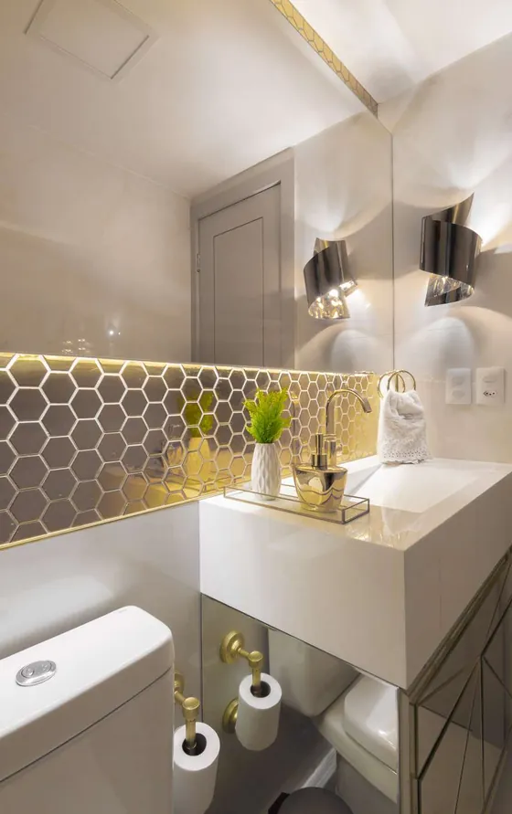 Lavabo com revestimento hexagonal dourado, bancada branca e arandelas