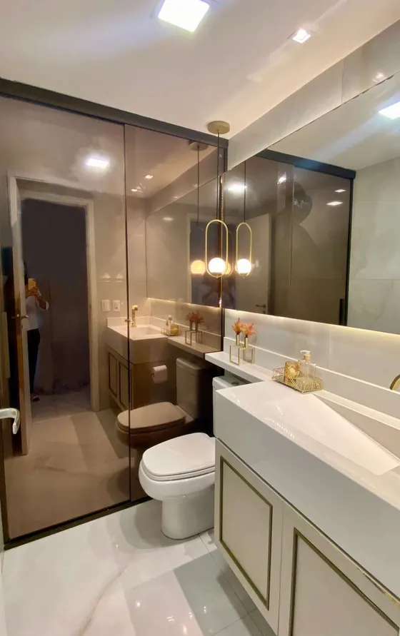 Banheiro com box de vidro, bancada branca e pendente dourado