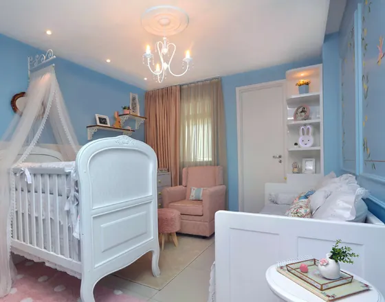 Quarto de bebê com parede azul, berço branco com dossel e lustre