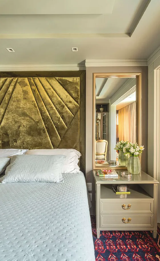 Quarto de casal com cabeceira dourada, criado-mudo claro e flores