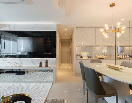 Sala integrada com mesa de jantar oval de tampo claro, cadeiras cinza, lustre dourado de globos e painel escuro de TV