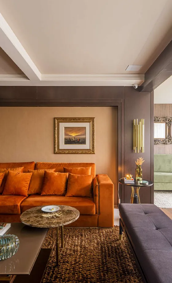 Sala de estar com sofá de veludo laranja, mesa de centro de pedra e quadro com moldura dourada