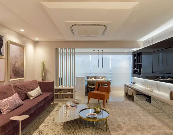 Sala de estar com sofá bordô, poltrona laranja, tapete claro e cozinha integrada ao fundo