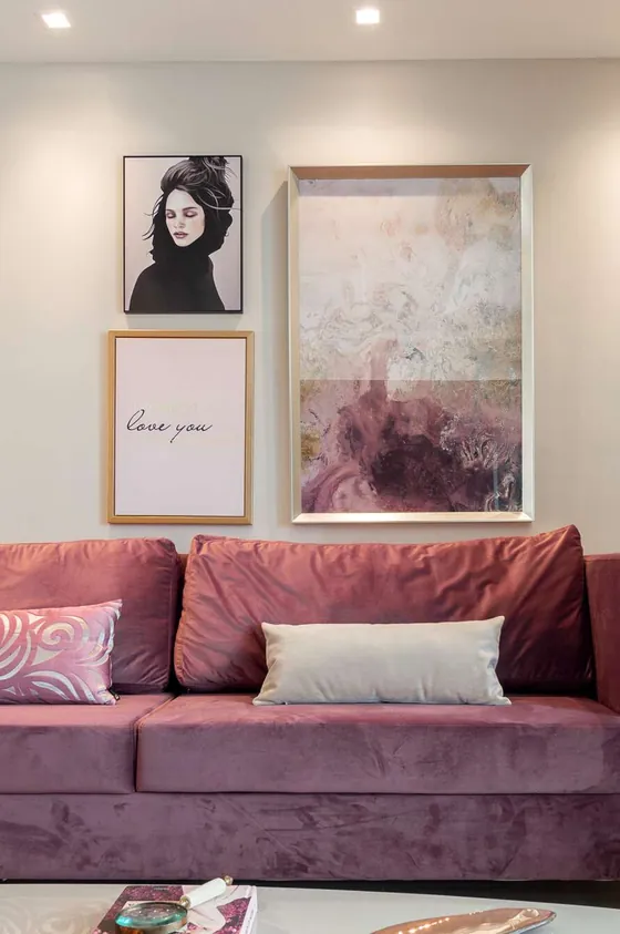 Sofá de veludo rosé com almofadas claras e quadros na parede