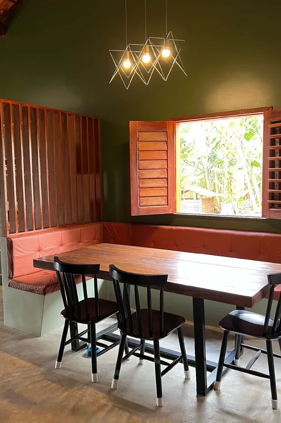 Sala de jantar com parede verde, banco estofado coral, mesa de madeira e cadeiras pretas