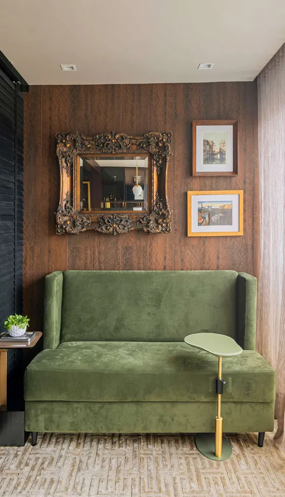 Varanda com sofá de veludo verde, painel de madeira e espelho de moldura dourada